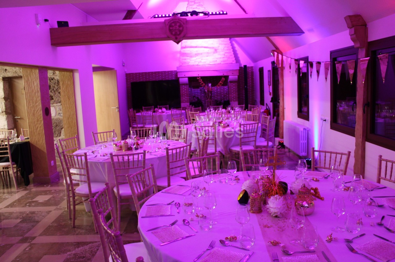 Salle de réception décorée avec des tables rondes dressées, éclairage rose et guirlandes suspendues.