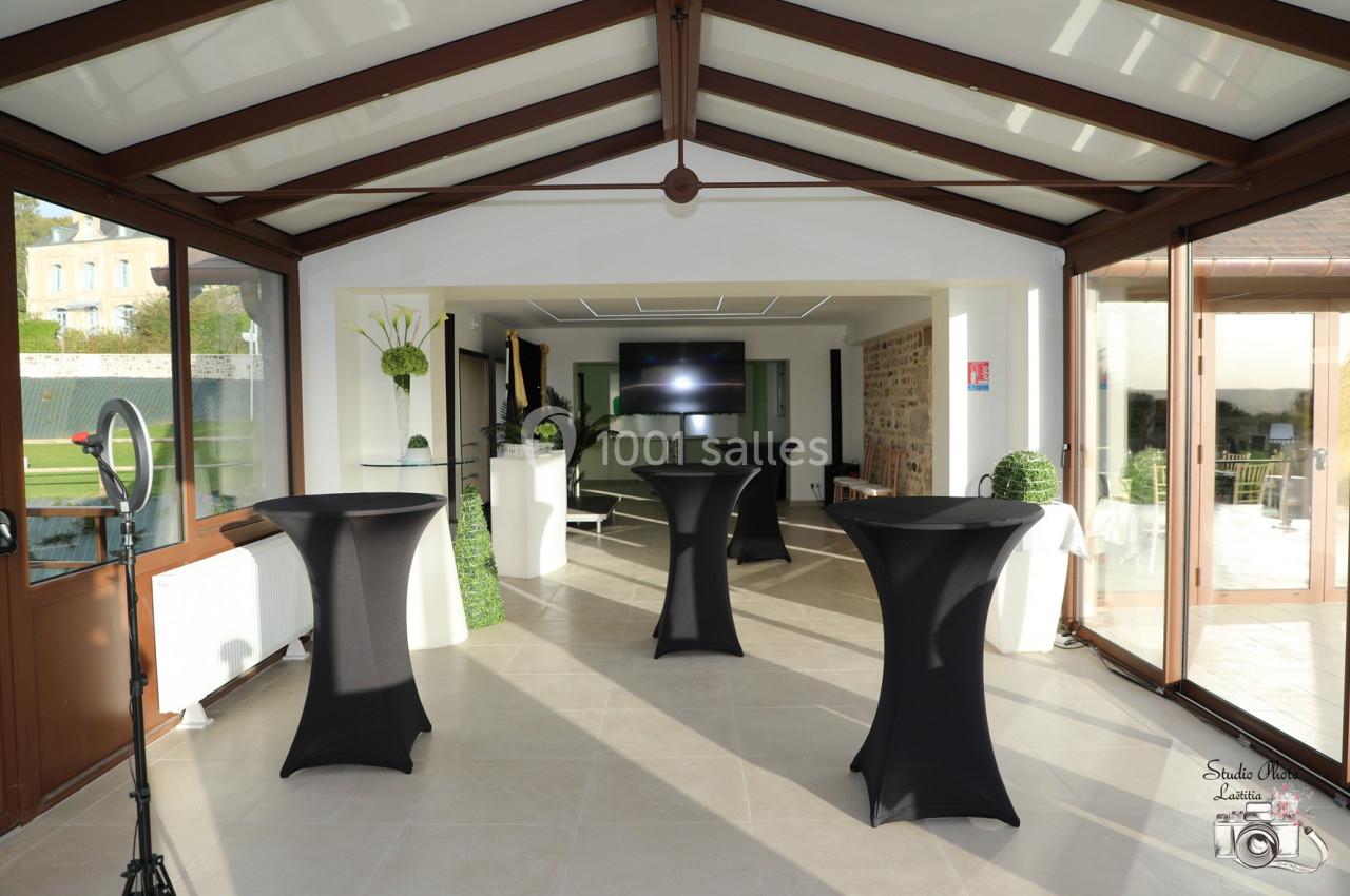 Location salle Saint-Samson-de-la-Roque (Eure) - Manoir Néo Normand #91 Salle lumineuse avec tables hautes noires, grandes baies vitrées, écran au fond et vue sur un jardin.