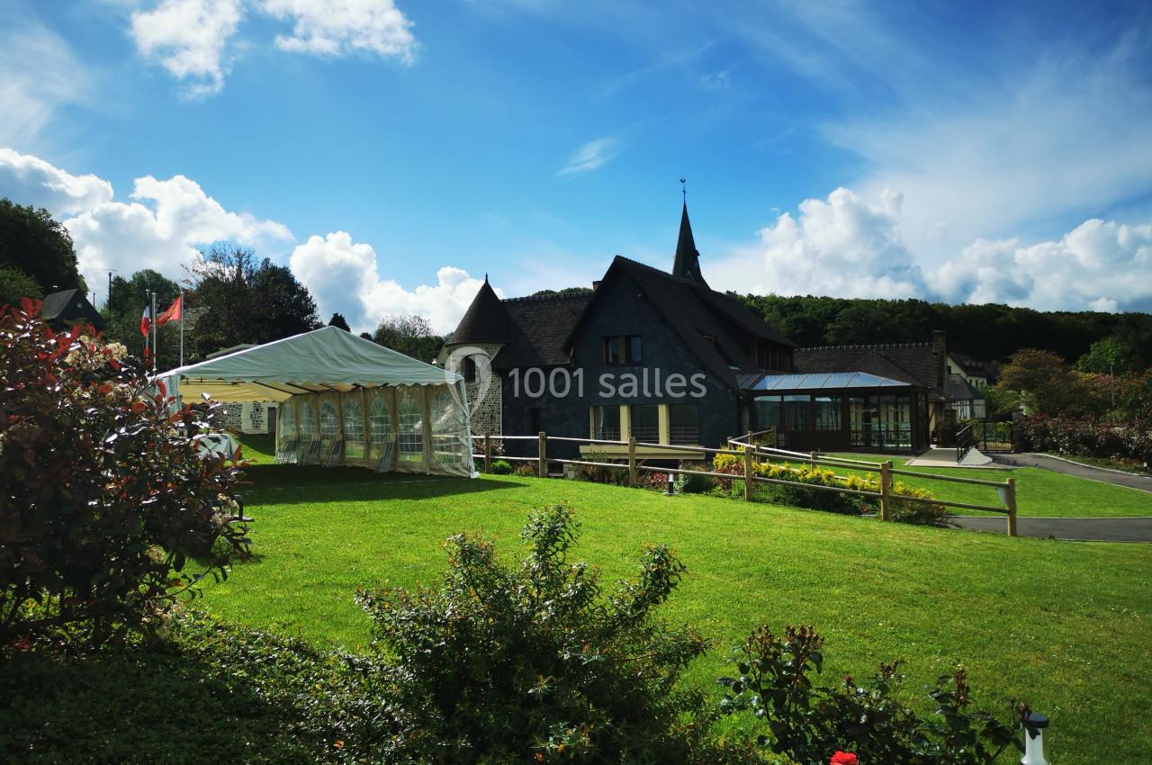 Location salle Saint-Samson-de-la-Roque (Eure) - Manoir Néo Normand #100 Jardin verdoyant avec pelouse, tente blanche, bâtiment en pierre et ciel bleu parsemé de nuages.
