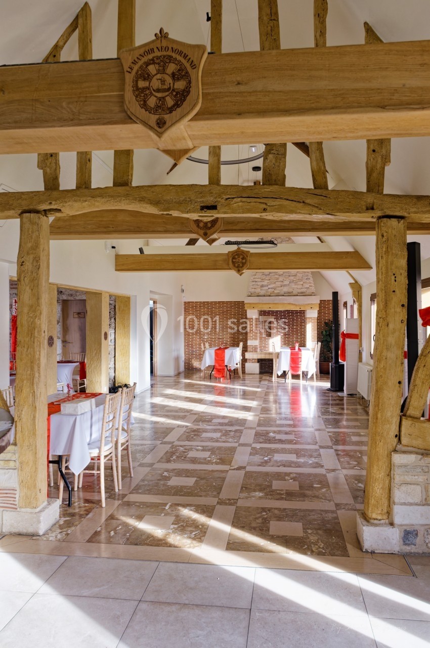 Salle lumineuse avec poutres en bois apparentes, tables dressées et sol en pierre naturelle.