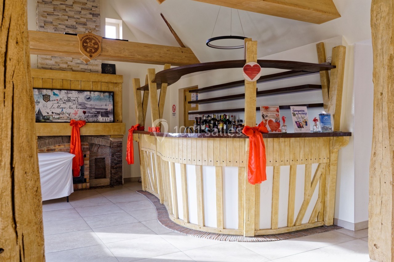 Bar en bois clair décoré de rubans rouges, situé dans une pièce lumineuse avec cheminée en pierre.