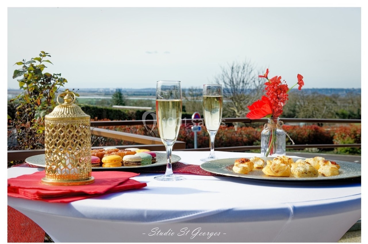 Table dressée en extérieur avec macarons, amuse-bouches, deux verres de champagne et une décoration florale rouge.