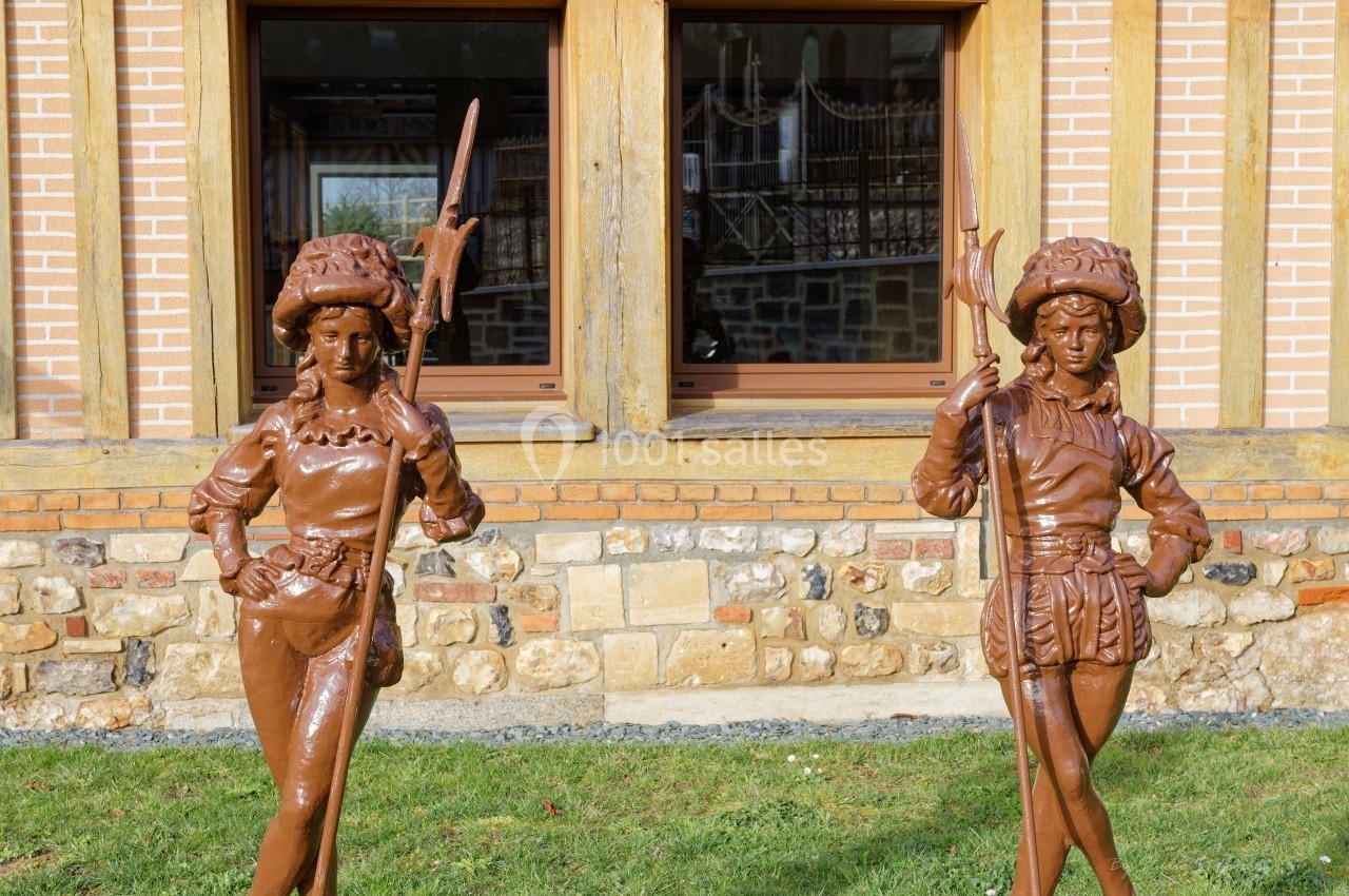 Location salle Saint-Samson-de-la-Roque (Eure) - Manoir Néo Normand #96 Deux statues en métal représentant des personnages médiévaux devant une façade en briques et pierres avec fenêtres.