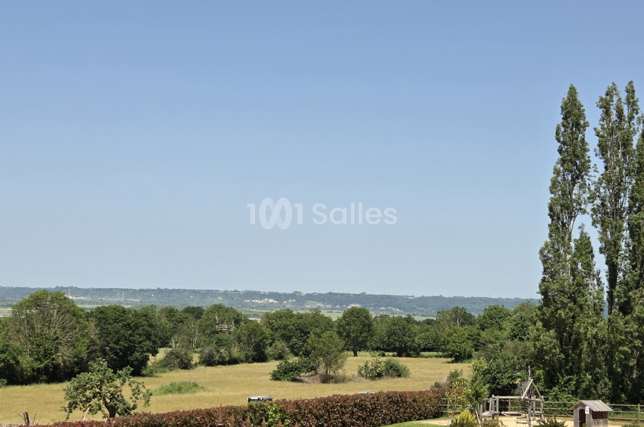 Parc paysagé avec vue panoramique sur les collines normandes boisées sous ciel dégagé.
