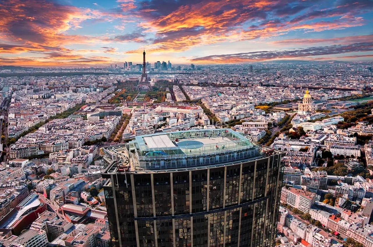 Vue aérienne de Paris au coucher du soleil, avec la Tour Montparnasse au premier plan et la Tour Eiffel en arrière-plan.