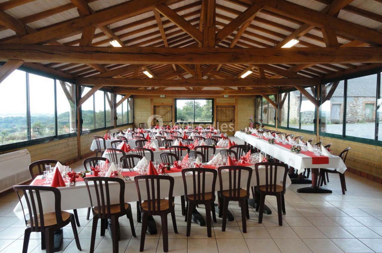 Salle de réception avec tables dressées, nappes blanches et décorations rouges, entourée de grandes baies vitrées.