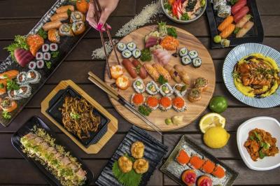 Assortiment varié de sushis, makis, sashimis et plats japonais disposés sur une table en bois sombre.