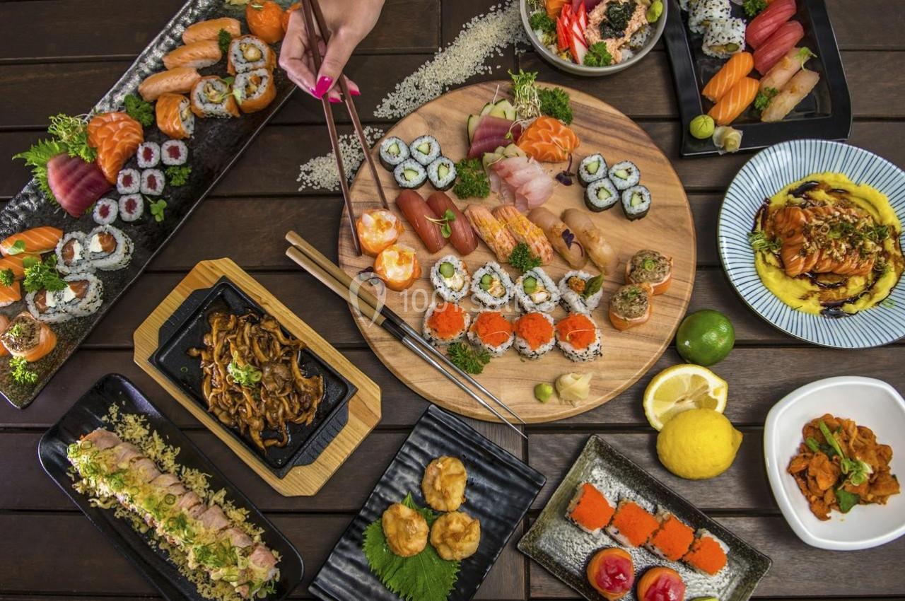 Assortiment varié de sushis, makis, sashimis et plats japonais disposés sur une table en bois sombre.