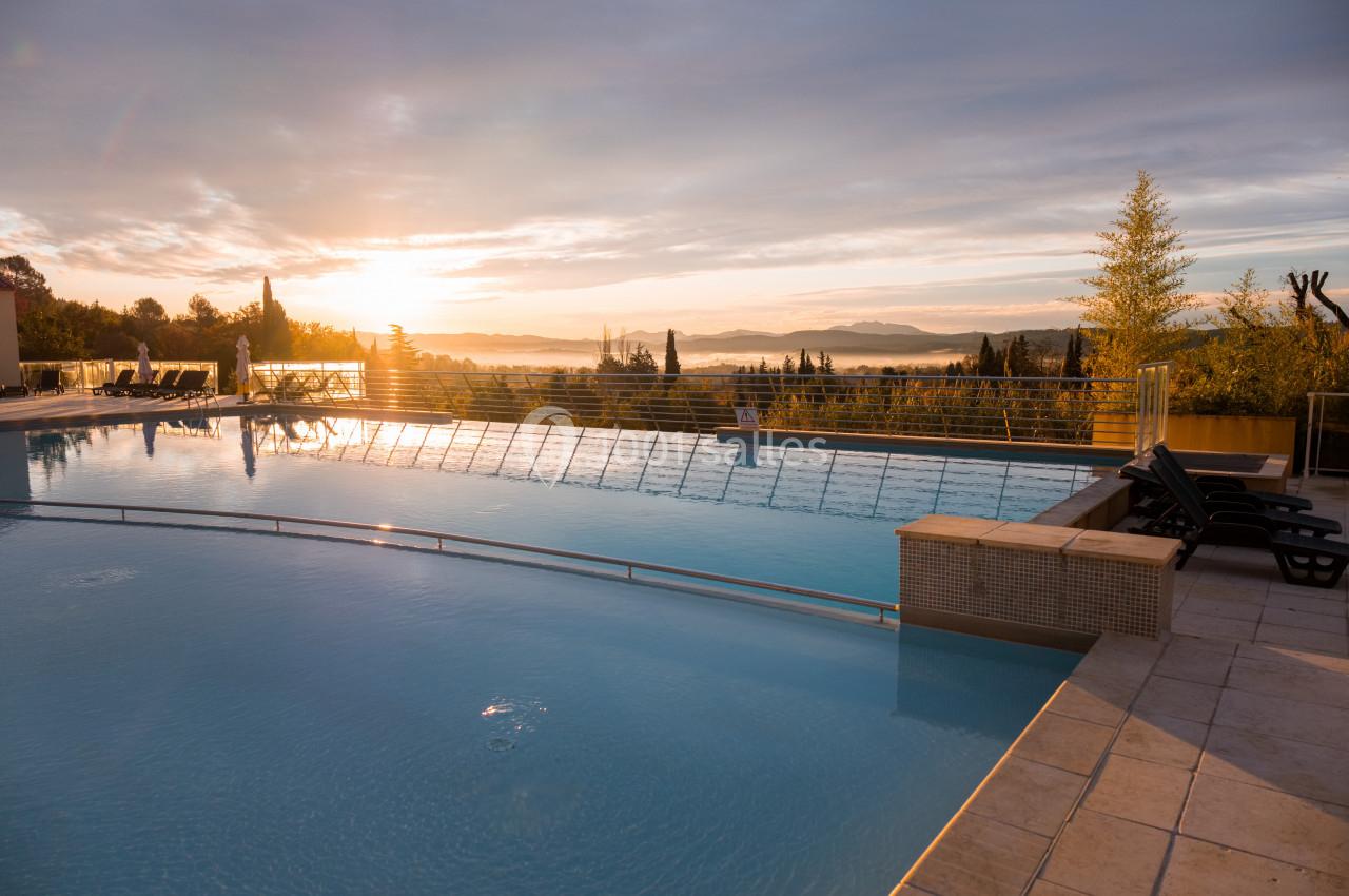 Piscine extérieure au lever du soleil, entourée de végétation et offrant une vue dégagée sur un paysage vallonné.
