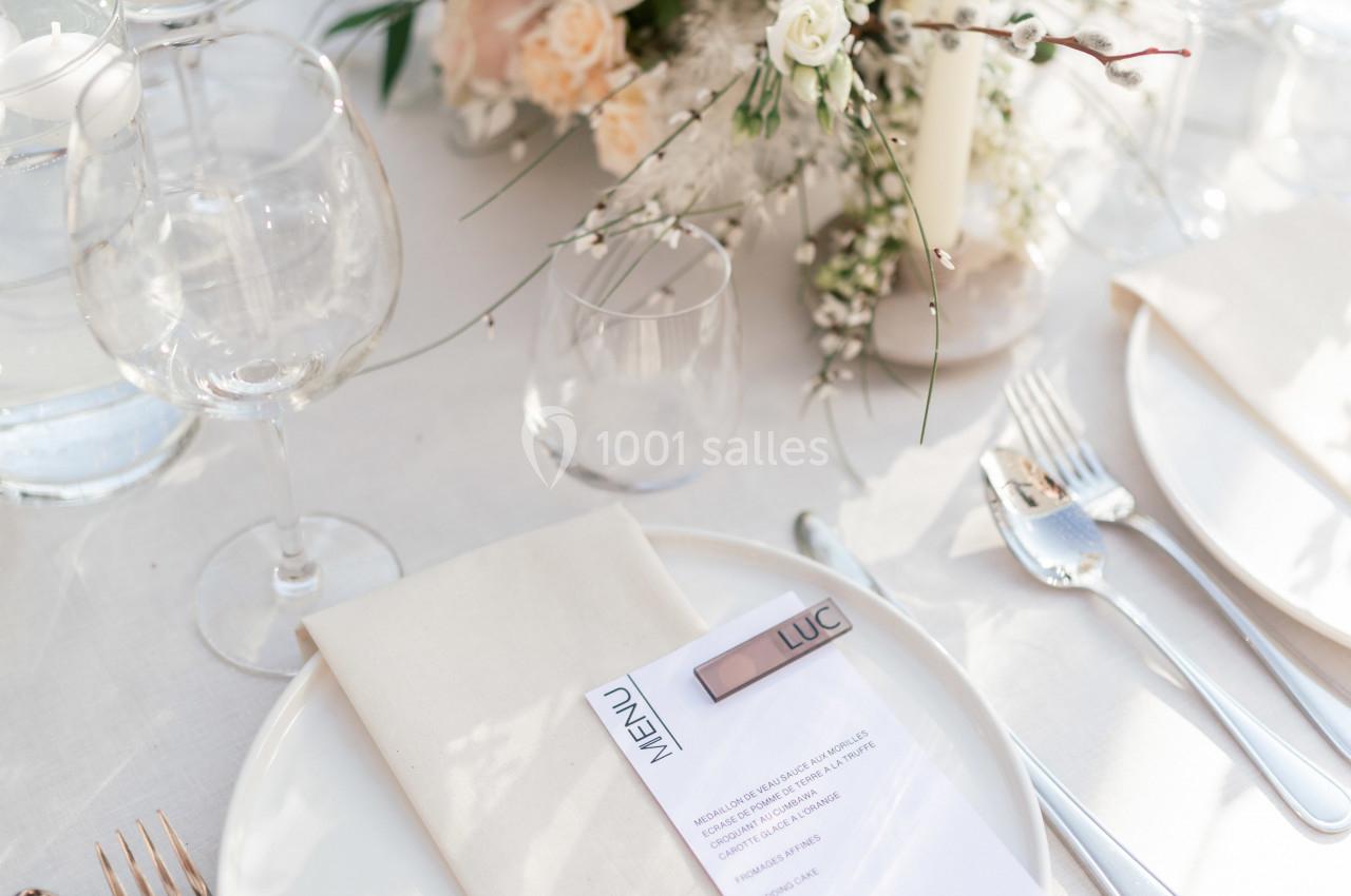 Table dressée avec élégance, comprenant des assiettes blanches, des couverts argentés, un menu et un centre de table floral.