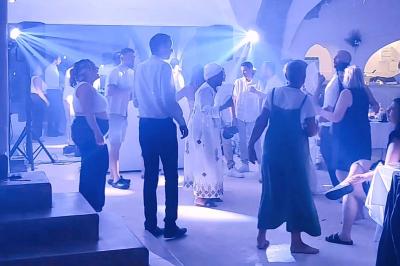Des personnes dansent dans une salle éclairée par des projecteurs, ambiance festive avec des invités en arrière-plan.