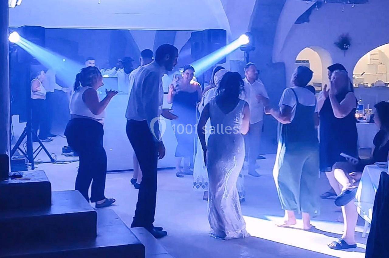 Des invités dansent dans une salle éclairée par des projecteurs bleus lors d'une fête ou d'un mariage.