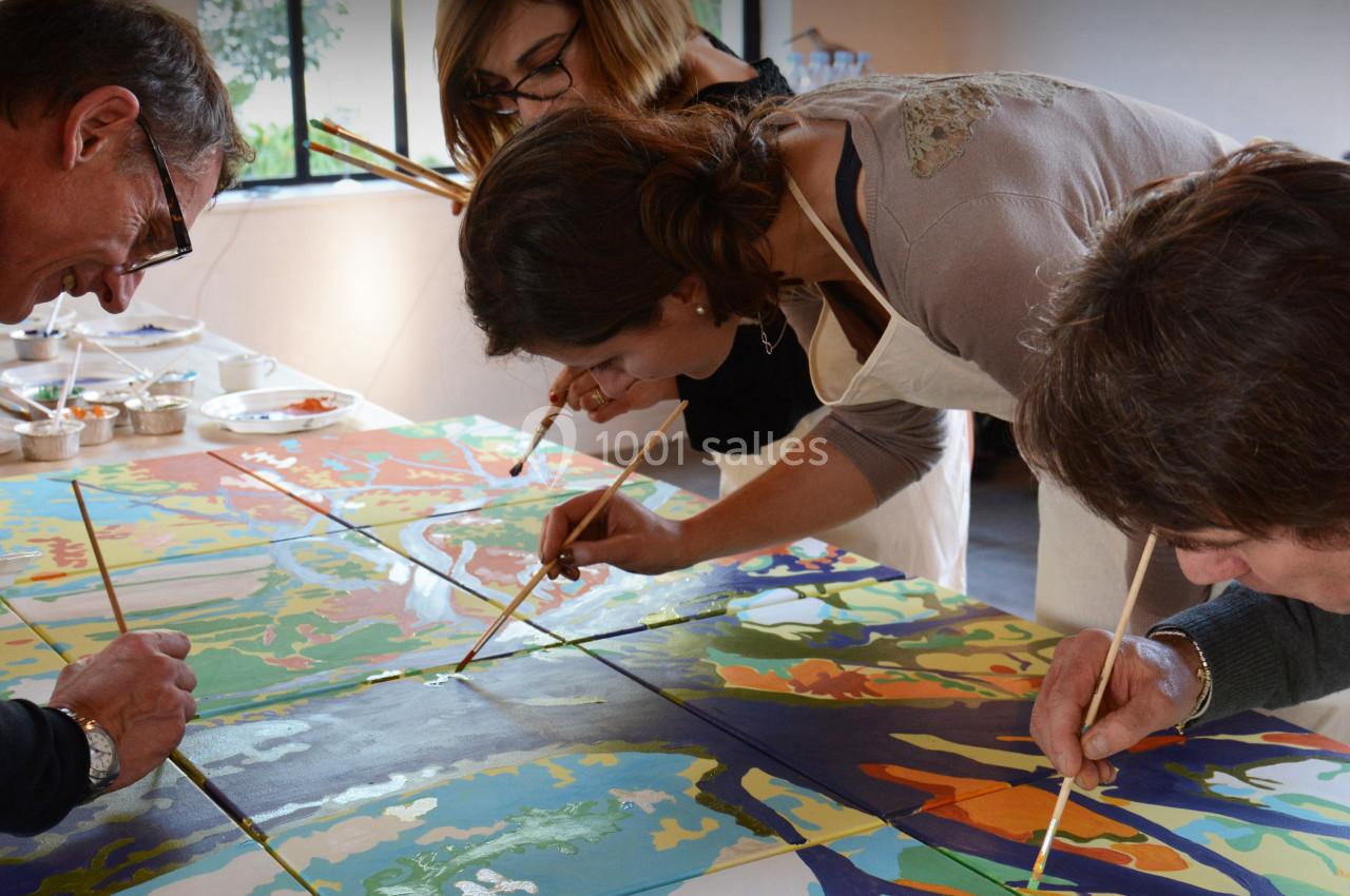 Des personnes concentrées peignent ensemble une grande fresque colorée sur une table dans un espace lumineux.