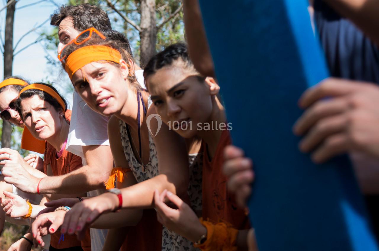 Des personnes en groupe, portant des bandeaux orange, semblent concentrées lors d'une activité en plein air.
