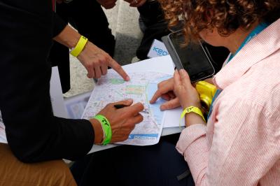 Deux personnes consultent une carte imprimée, l'une pointant un lieu précis tandis que l'autre prend des notes.