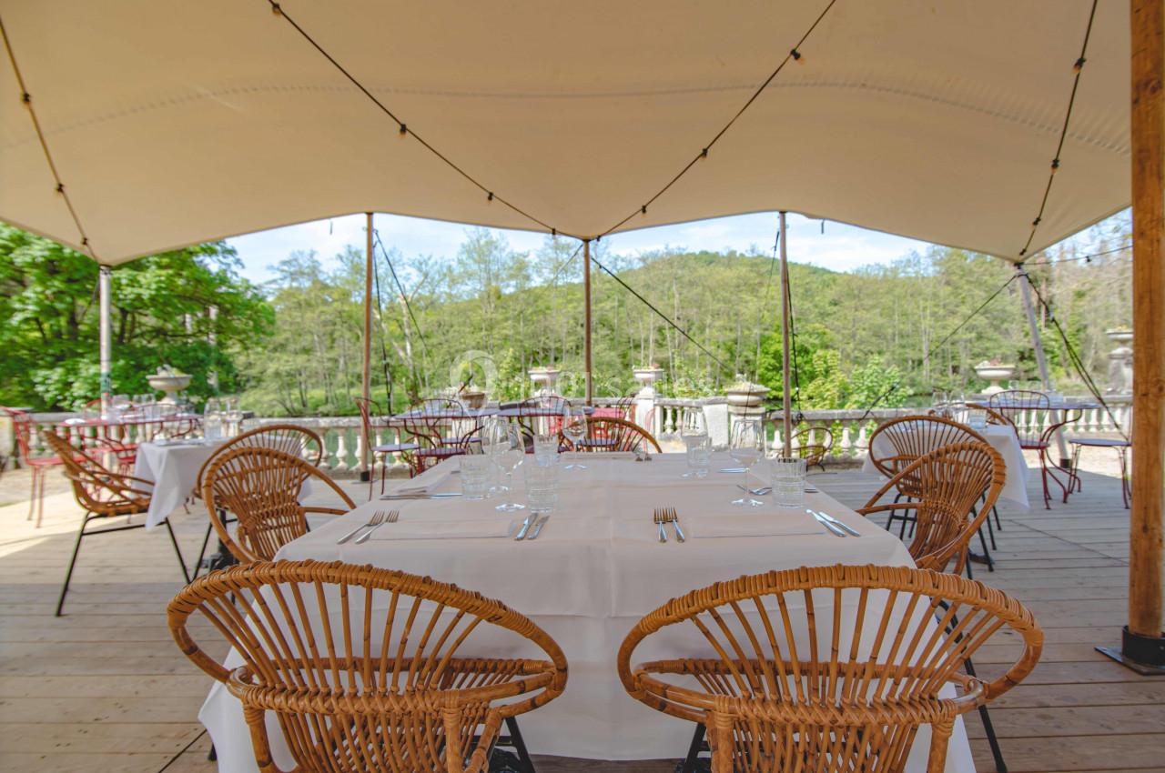 Terrasse extérieure avec tables dressées sous une tente, entourée de verdure et offrant une vue sur la nature.