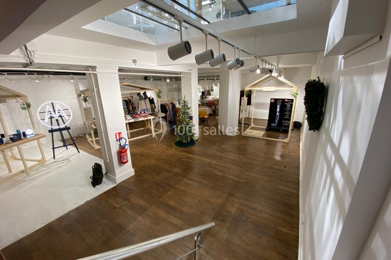 Espace intérieur lumineux avec parquet, stands d'exposition, sapin décoré et éclairage suspendu.