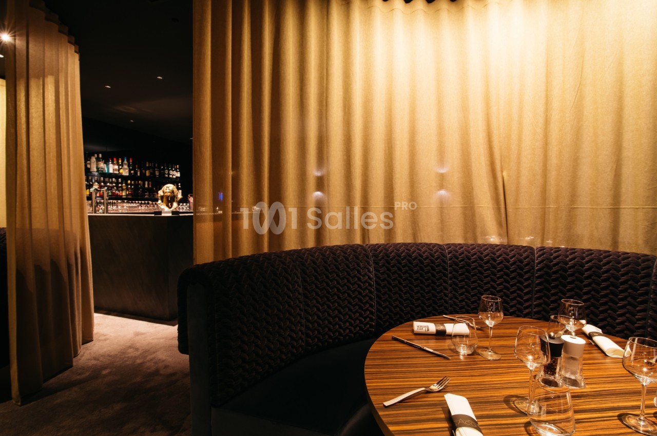 Banquette arrondie avec table dressée dans un restaurant élégant, éclairage tamisé et rideaux dorés en arrière-plan.