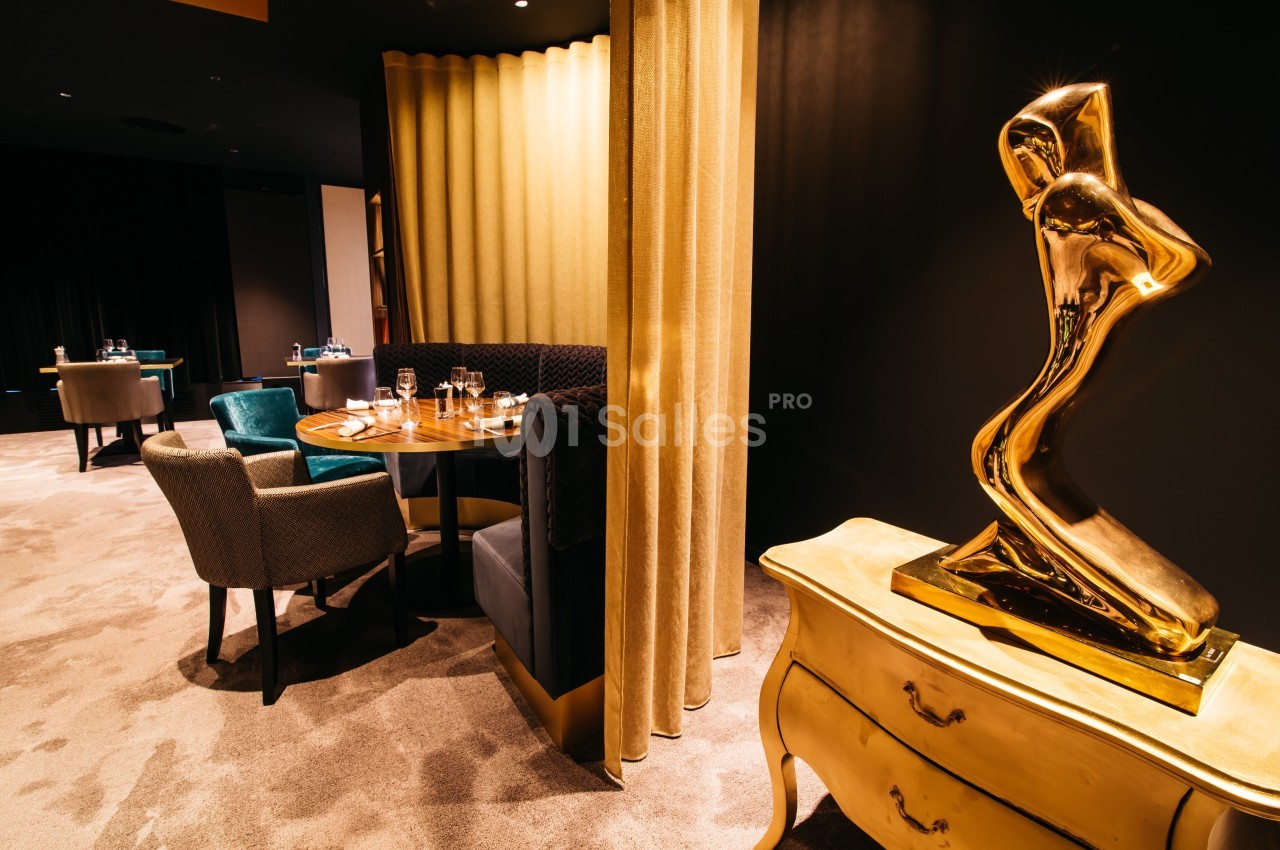 Salle de restaurant élégante avec des tables dressées, des fauteuils colorés et une sculpture dorée sur une commode.