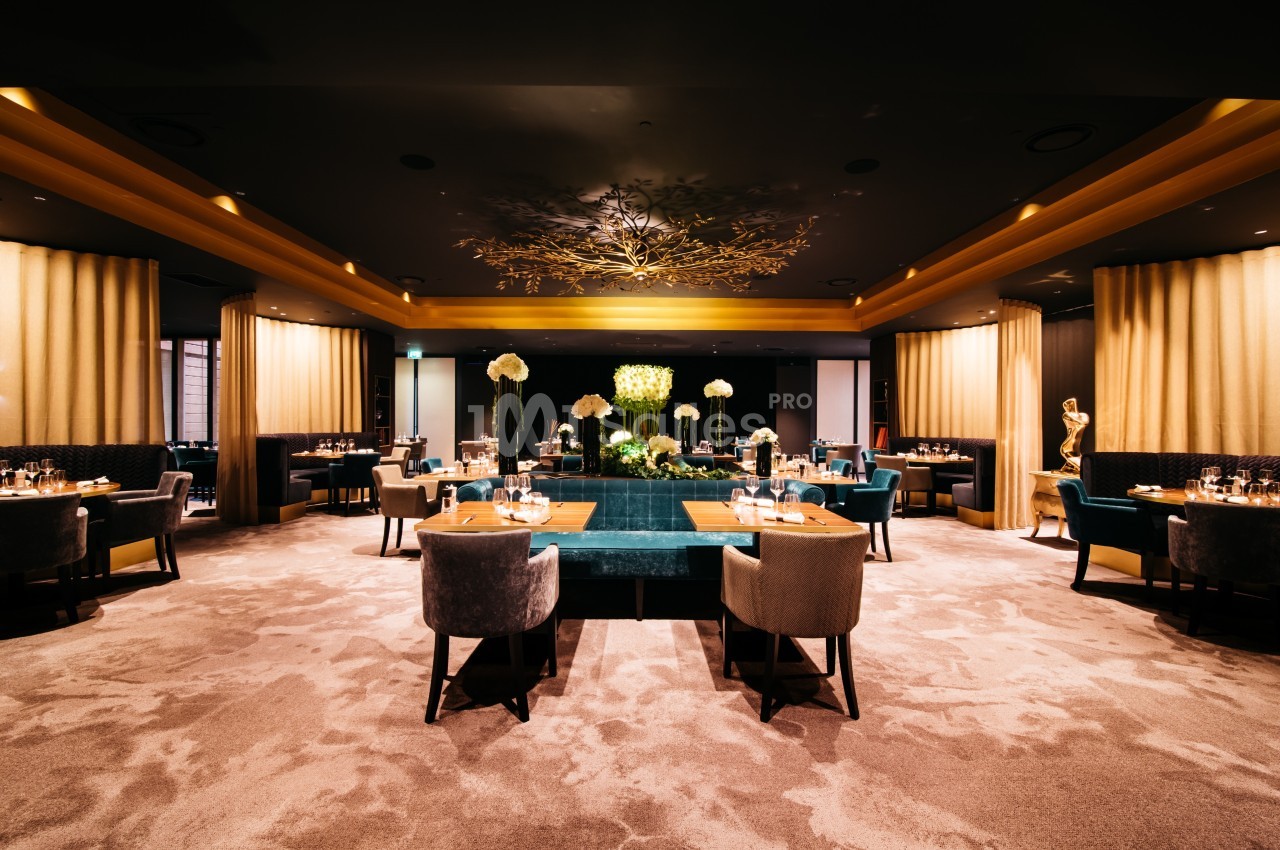 Salle de restaurant élégante avec tables dressées, éclairage tamisé et décoration florale au centre.