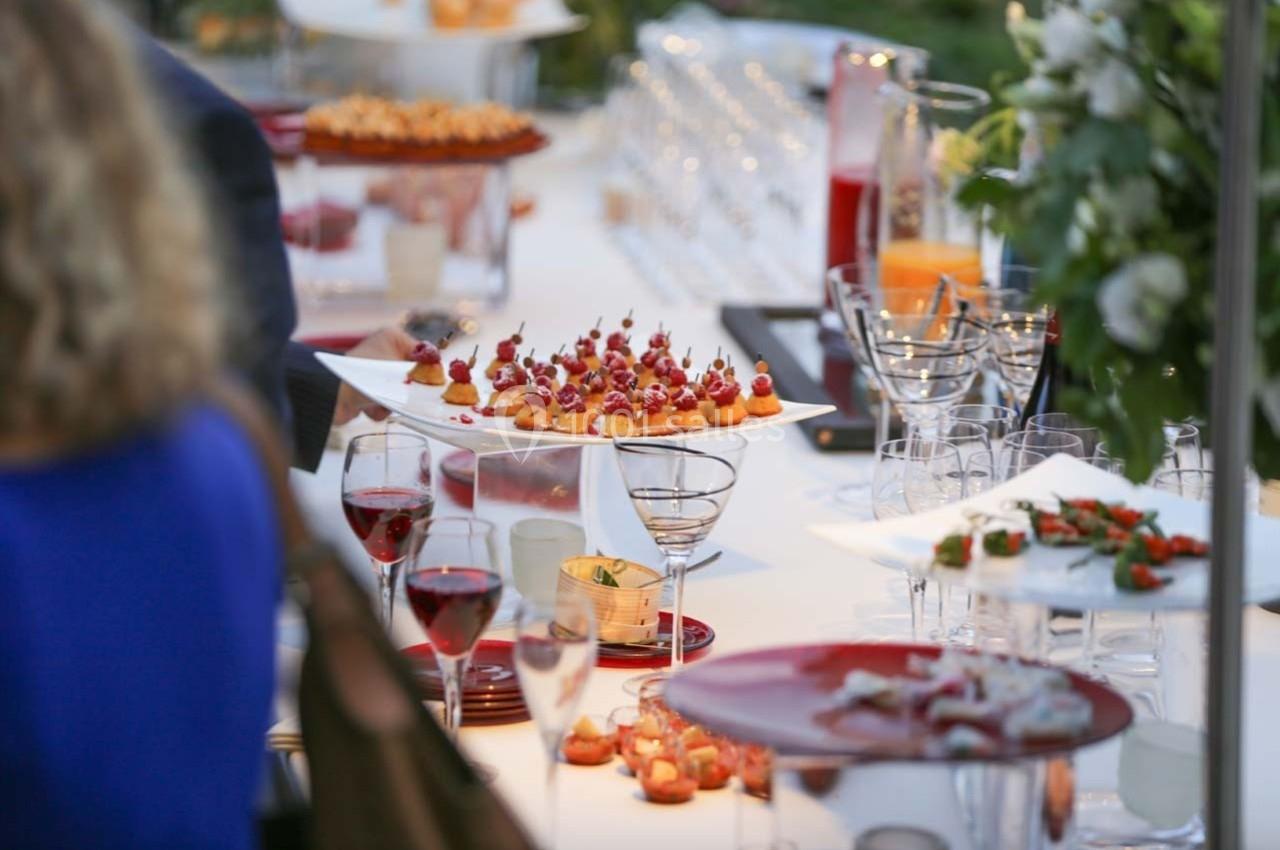 Table dressée avec des amuse-bouches variés, verres de vin rouge et décoration florale en arrière-plan.