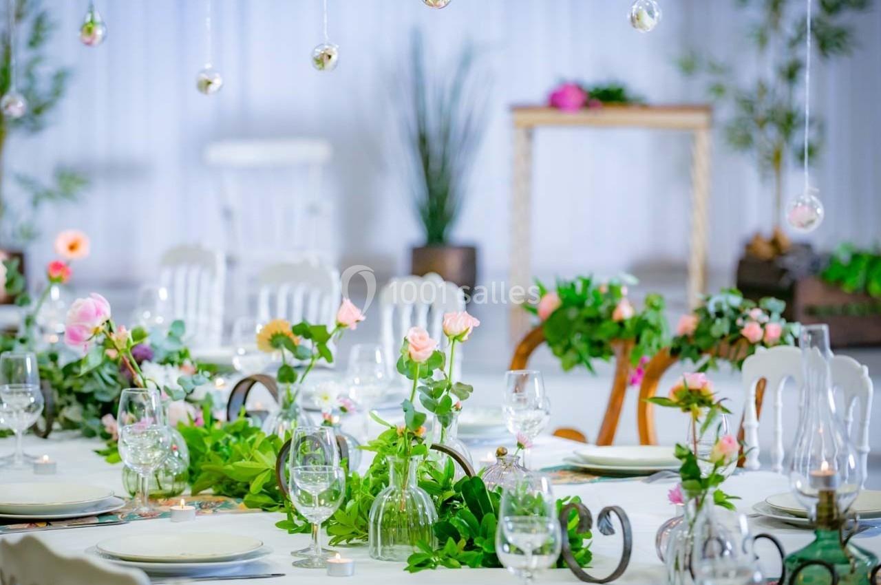 Table décorée avec des fleurs roses et vertes, vaisselle élégante et ambiance lumineuse dans un cadre raffiné.