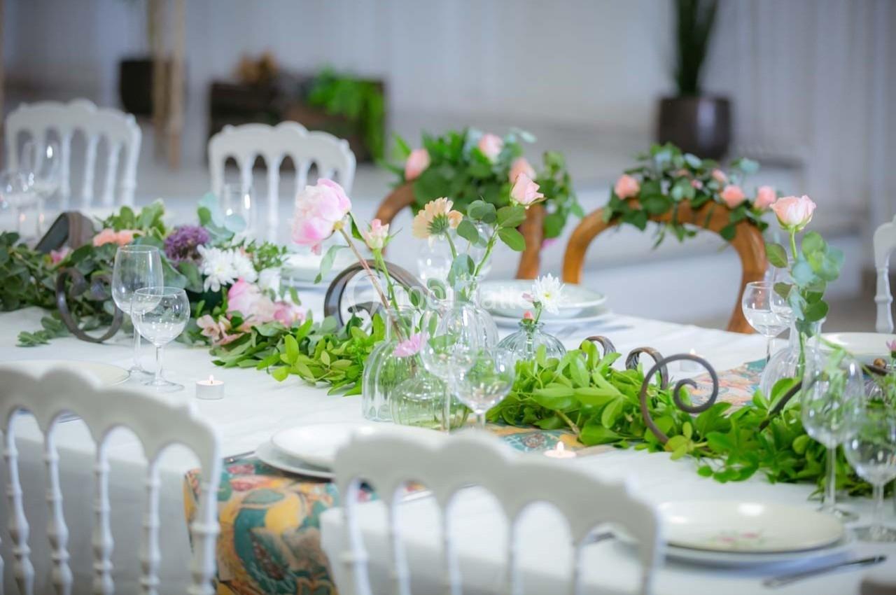 Table décorée avec des fleurs fraîches, feuillage vert, bougies et vaisselle blanche dans une ambiance élégante.