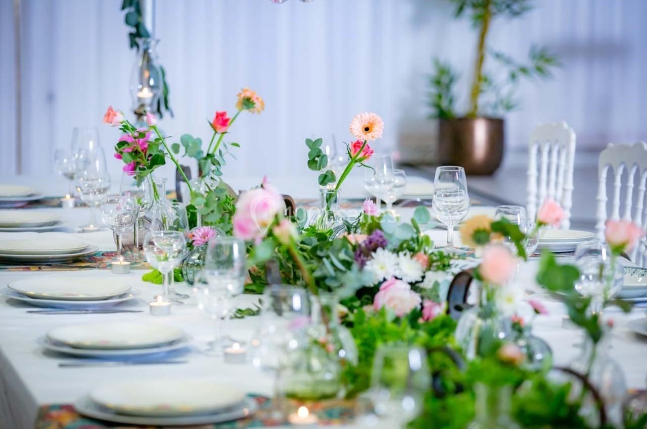 Table élégamment dressée avec des fleurs colorées, des verres et des assiettes, dans un décor lumineux et raffiné.