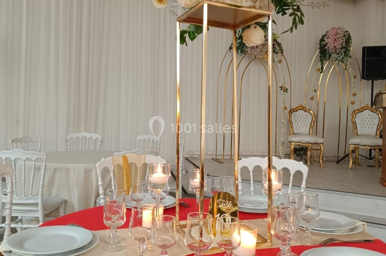 Table décorée pour un événement avec bougies, vaisselle élégante et centre de table floral sur une structure dorée.