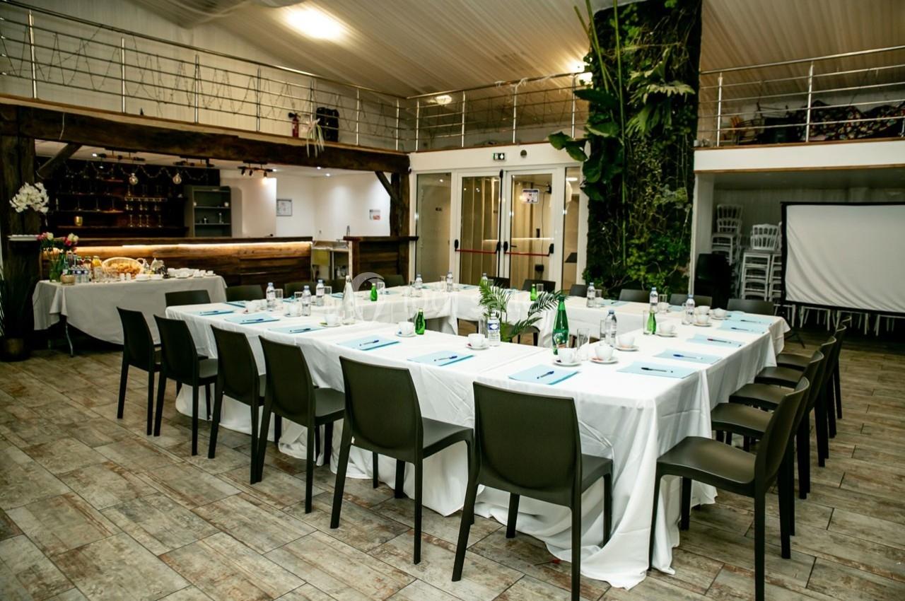 Salle aménagée pour une réunion avec des tables en U, nappes blanches, chaises noires et décor végétal en arrière-plan.