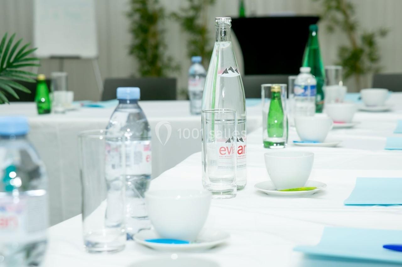 Bouteilles d'eau, tasses et documents disposés sur des tables blanches dans une salle de réunion lumineuse.