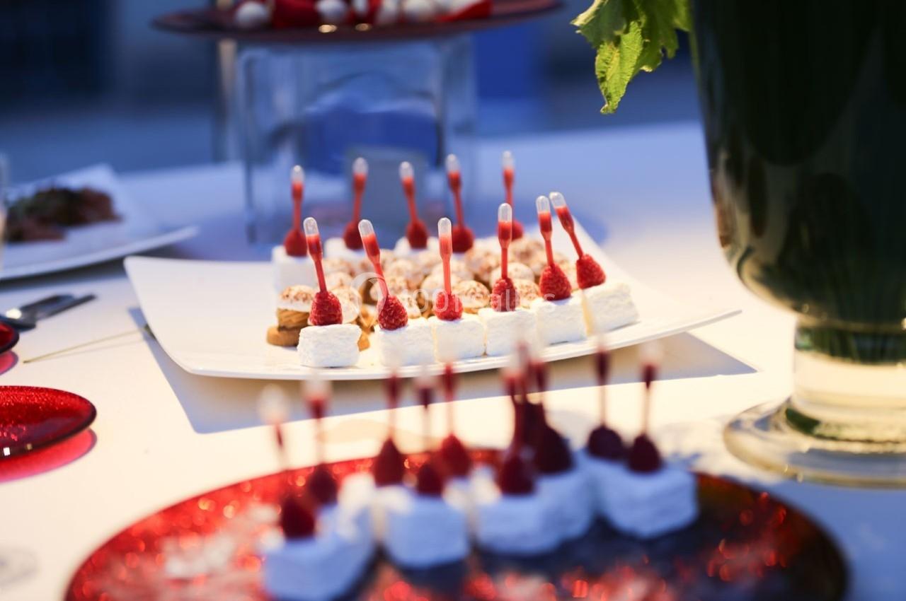 Assortiment de bouchées sucrées décorées de framboises et de pipettes, présenté sur des plateaux lors d'un événement.