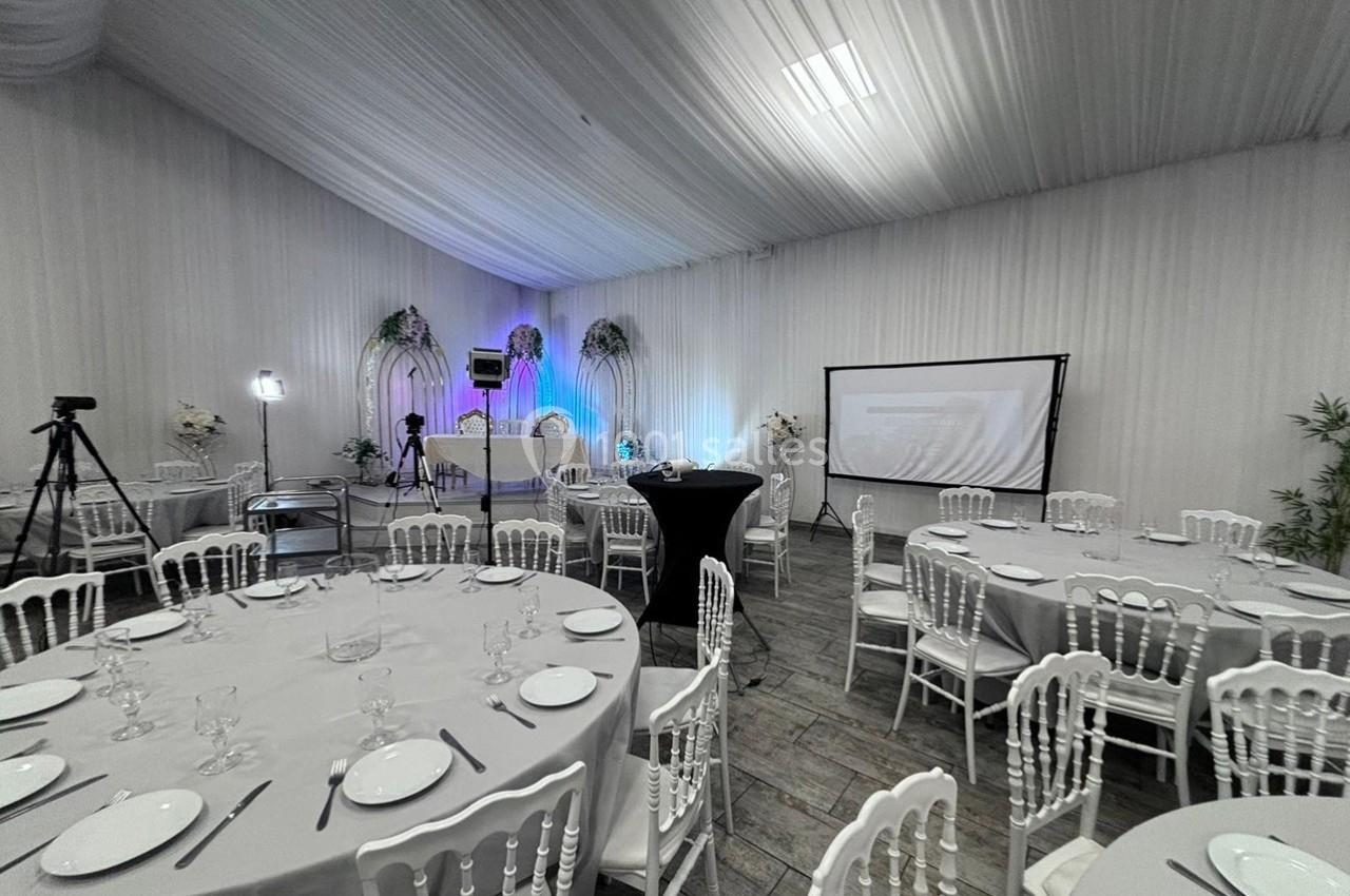 Salle de réception décorée avec des tables rondes dressées, un écran de projection et un éclairage coloré.
