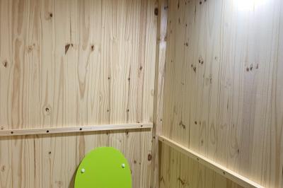 Toilettes sèches en bois clair avec abattant vert, éclairées par une lampe fixée au mur.