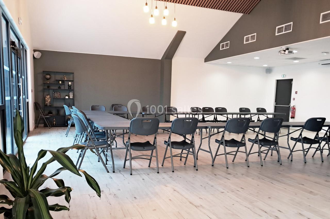 Salle de réunion lumineuse avec des tables disposées en U, des chaises pliantes et une décoration sobre.