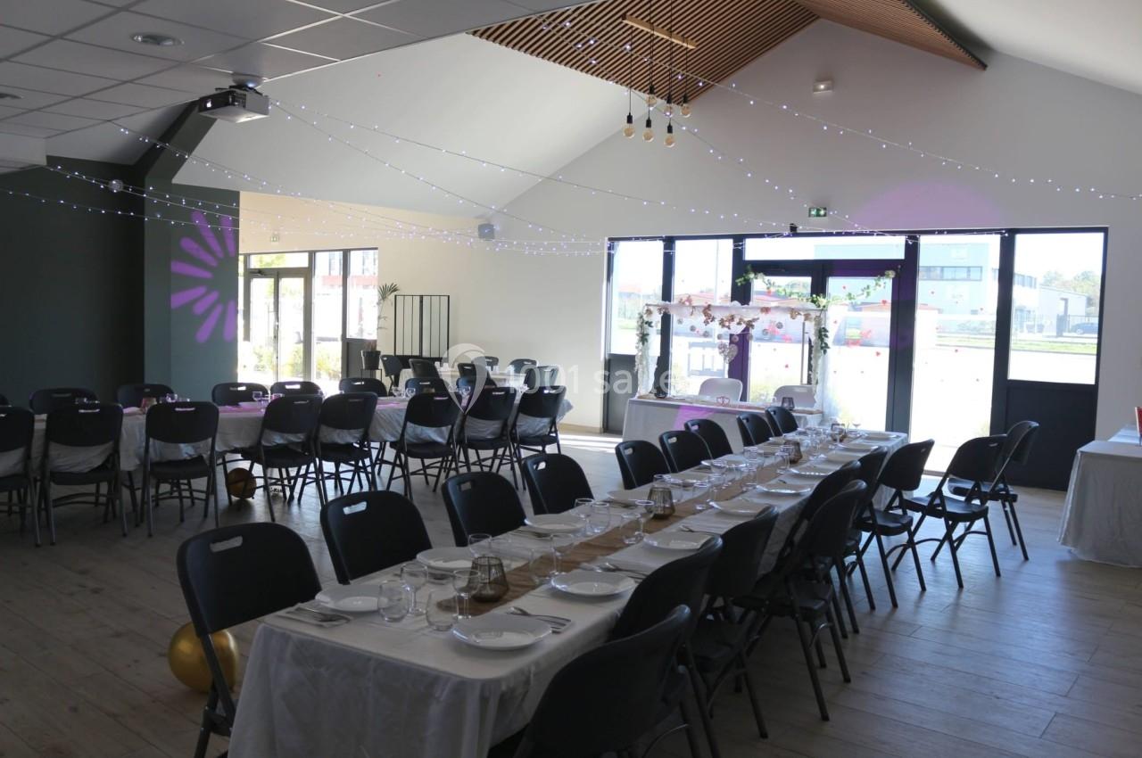 Salle de réception décorée avec des tables dressées, guirlandes lumineuses suspendues et lumière naturelle entrant par les…