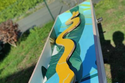 Planche de jeu de lancer de sacs colorée posée sur une pelouse, avec des sacs verts et jaunes dispersés autour.