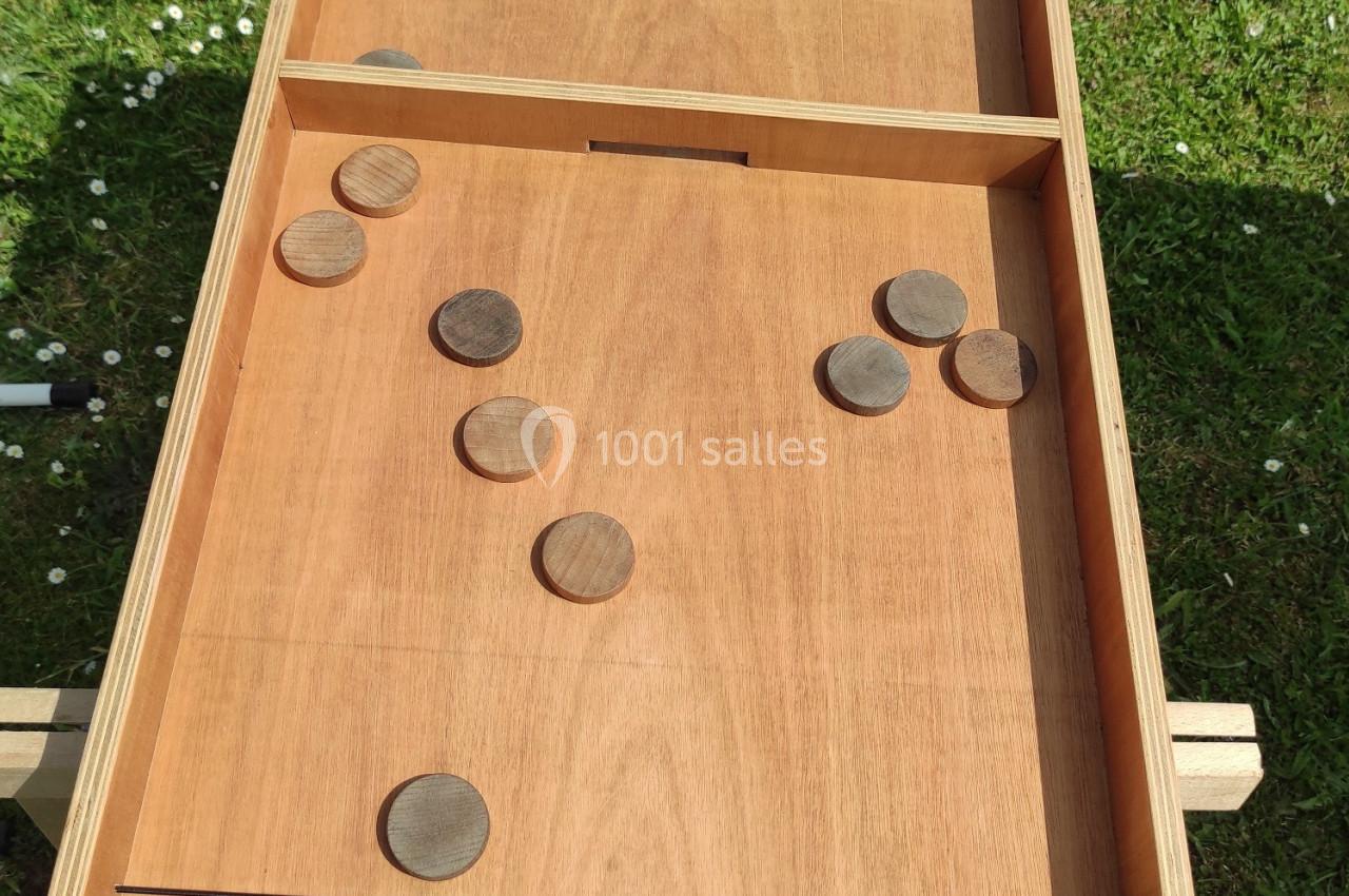 Jeu de passe-trappe en bois posé sur l'herbe, avec des palets répartis sur le plateau.