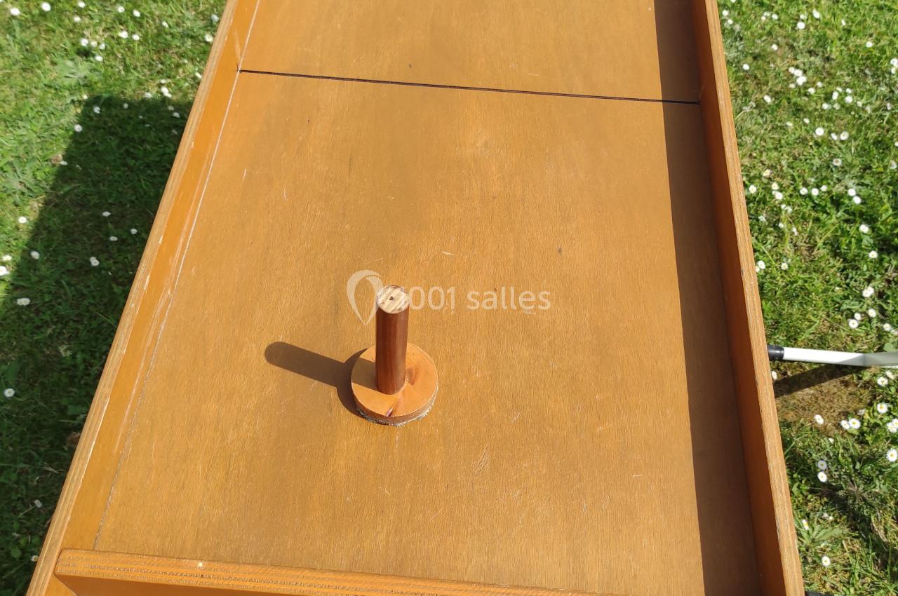 Jeu en bois traditionnel avec deux manches et un palet, posé sur une pelouse en extérieur.