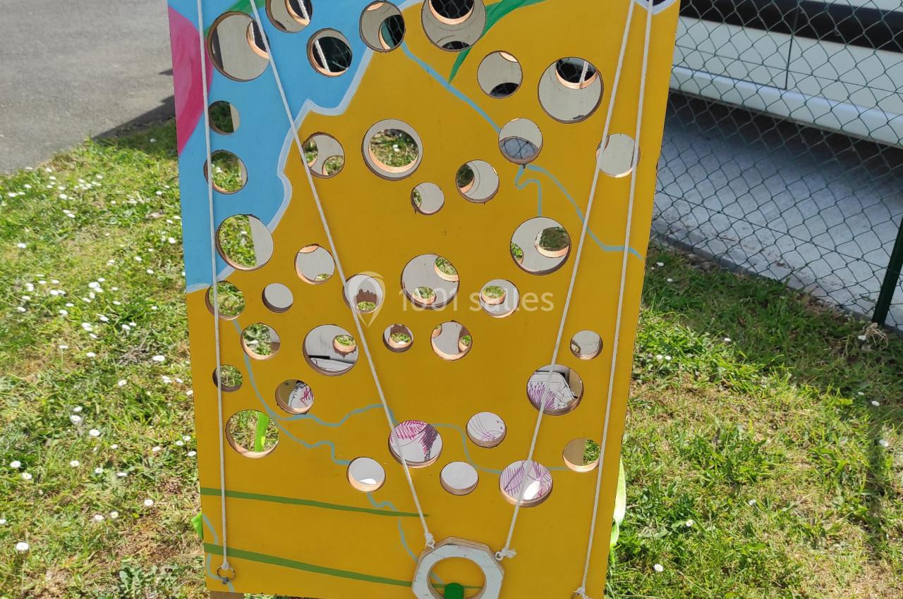 Panneau en bois coloré avec des trous de différentes tailles, utilisé pour un jeu d'adresse en extérieur.