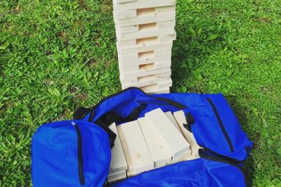 Planche de jeu de lancer de sacs colorée posée sur une pelouse, avec des sacs verts et jaunes dispersés autour.