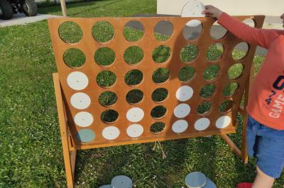 Planche de jeu de lancer de sacs colorée posée sur une pelouse, avec des sacs verts et jaunes dispersés autour.