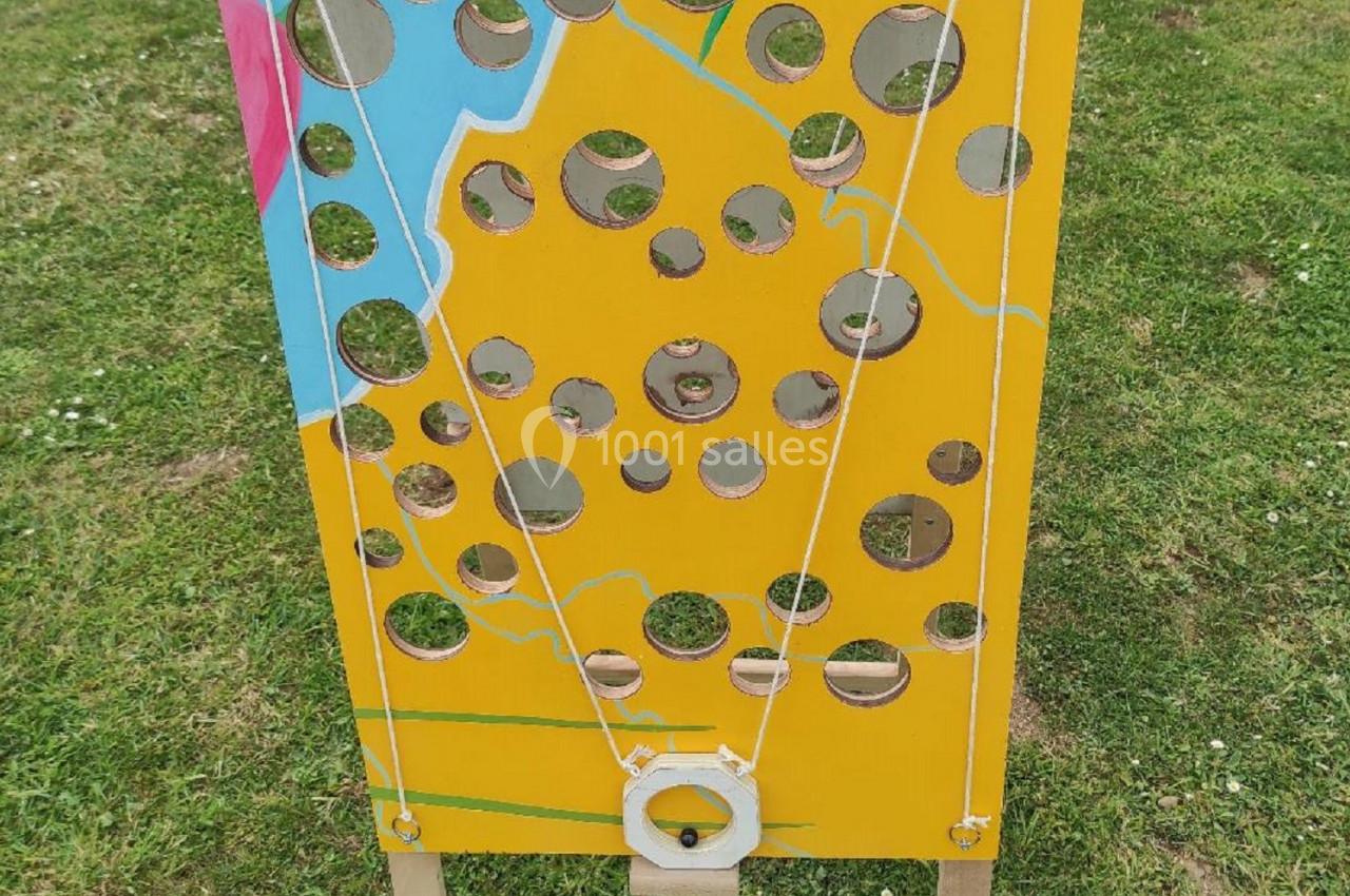 Panneau de jeu en bois jaune avec des trous de différentes tailles, posé sur une pelouse.