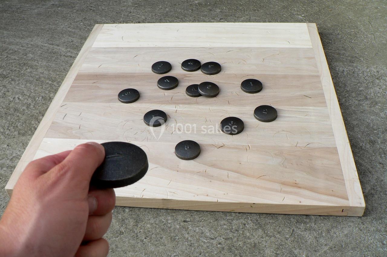 Main tenant un palet en pierre devant un plateau en bois avec plusieurs palets disposés dessus.