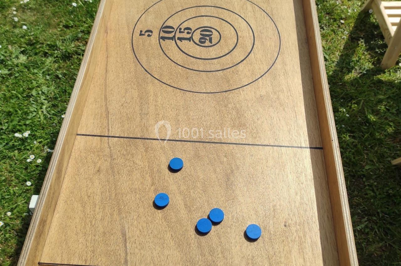 Jeu de palets en bois installé sur une pelouse, avec des palets bleus et gris dispersés sur la surface de jeu.