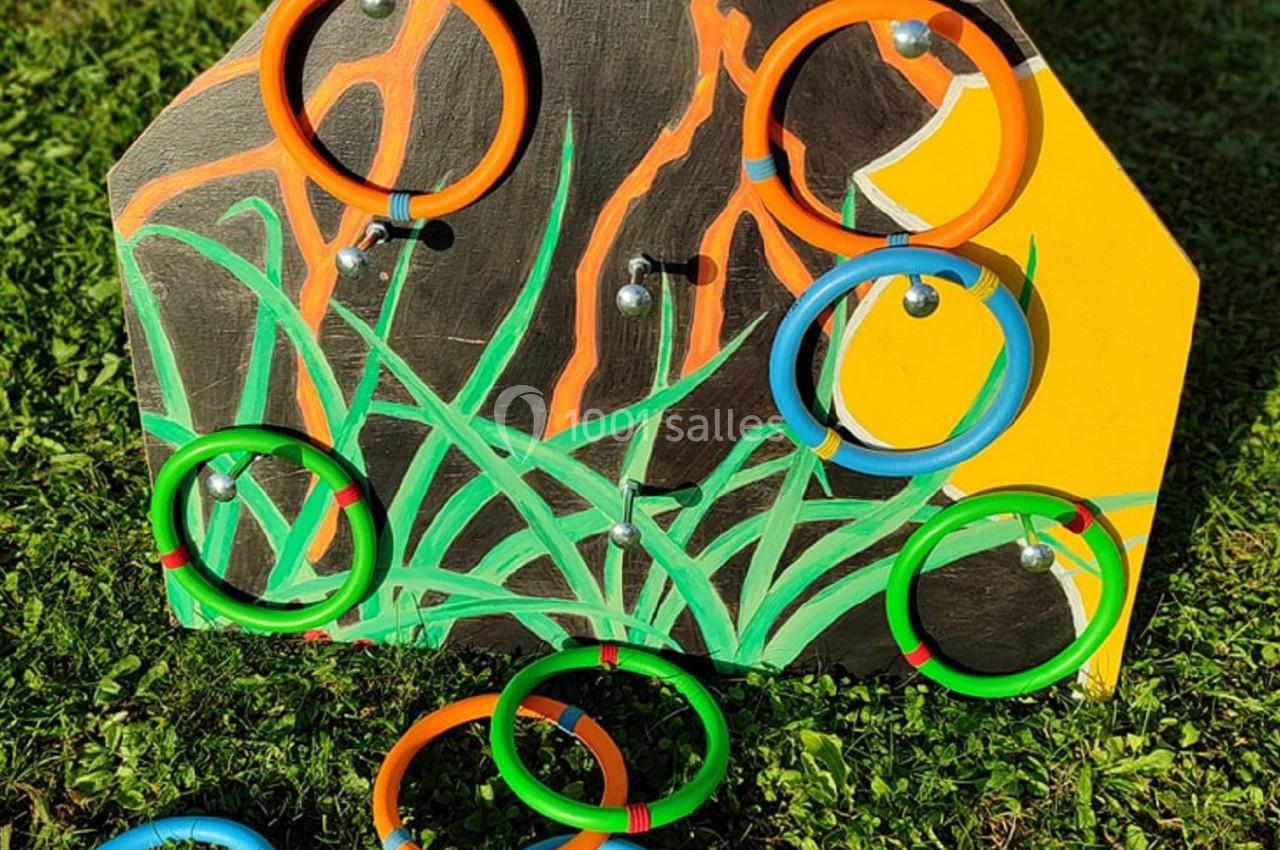 Panneau en bois coloré avec des anneaux multicolores accrochés et posés sur de l'herbe.