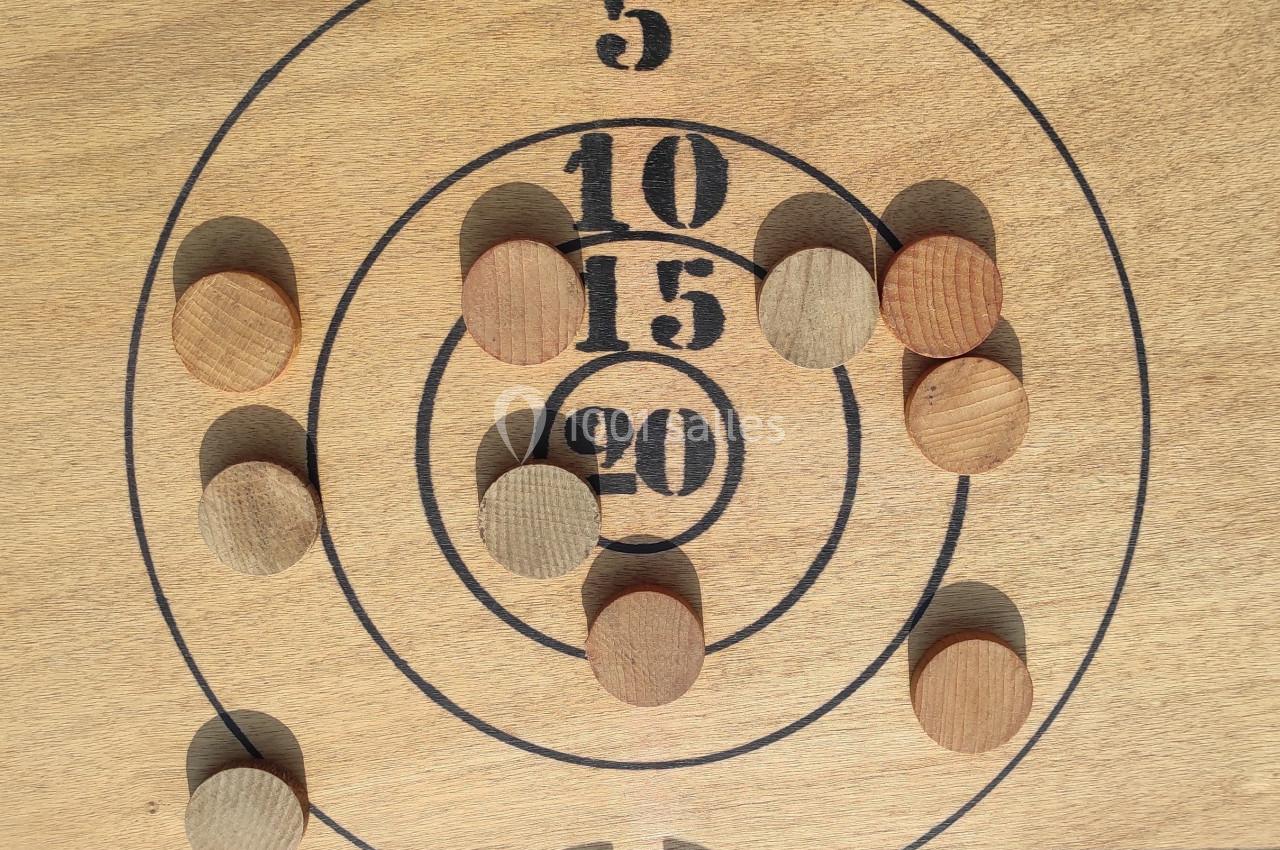 Disque en bois avec des cercles numérotés et des pions en bois disposés sur différentes zones de points.