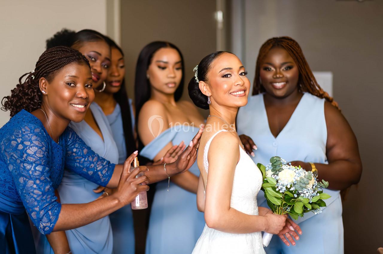 Une mariée souriante entourée de ses demoiselles d'honneur en robes bleues, ajustant sa tenue et tenant un bouquet.