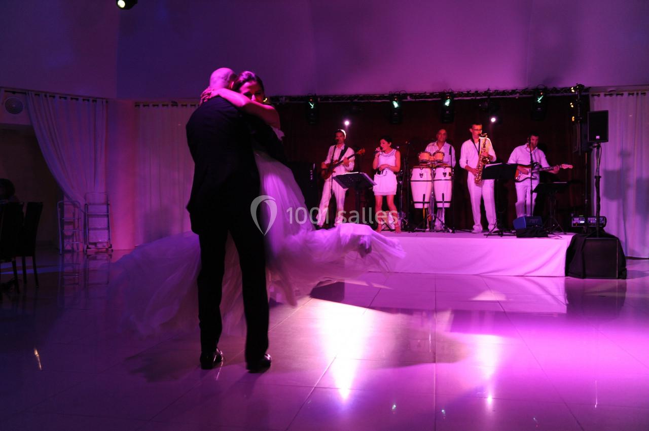 Un couple danse sous des lumières tamisées devant un groupe de musiciens sur scène.