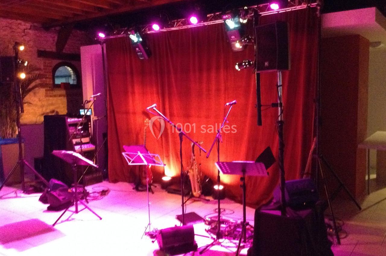 Scène de concert avec rideau rouge, micros sur pieds, pupitres et éclairage violet dans une salle intérieure.